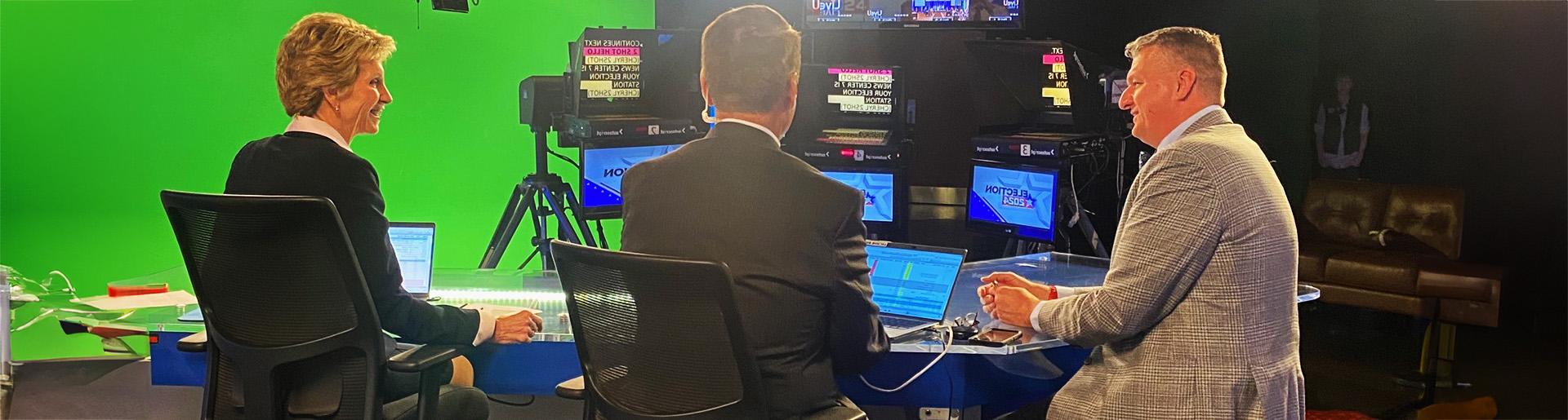 Dr. Mark Caleb Smith sitting behind news desk with news anchor giving an interview.